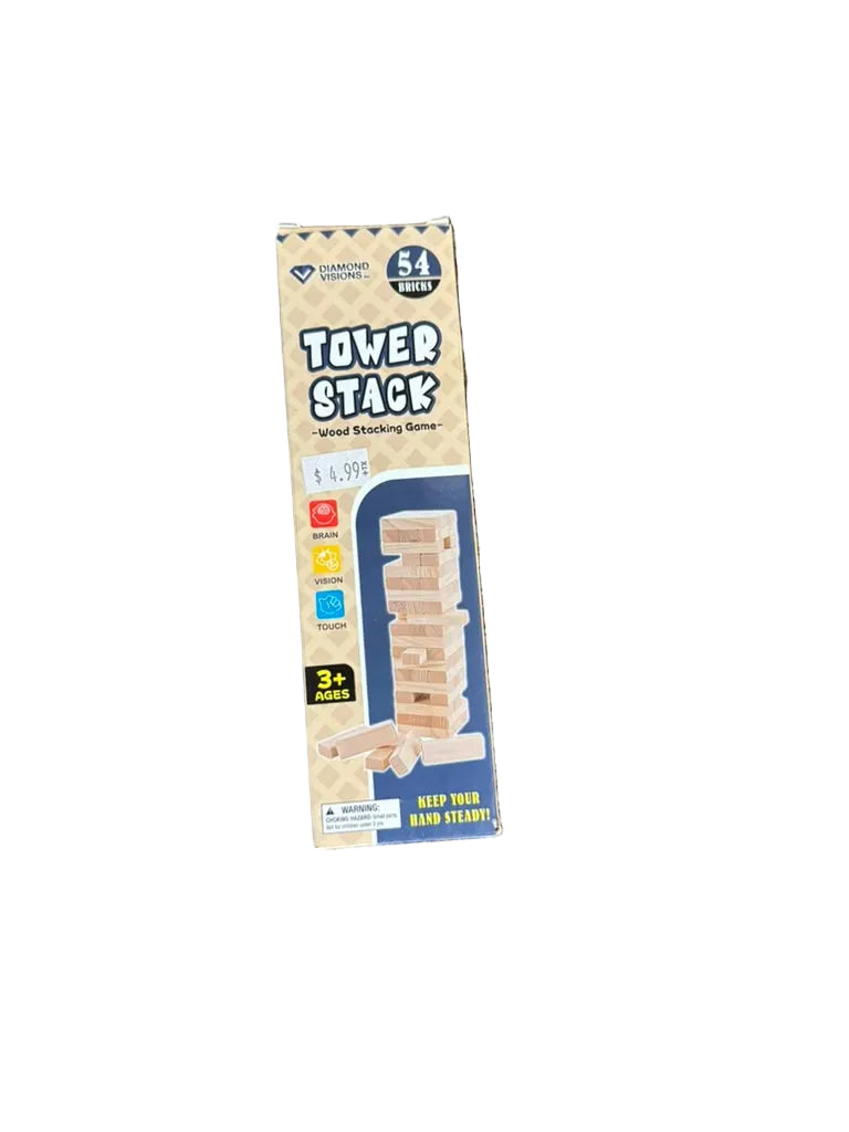 A boxed Tower Stack card game set standing upright on a textured carpeted floor. The package is beige with blue panels and shows a stack of wooden blocks, with product text including 'Tower Stack' and 'Card Game'.